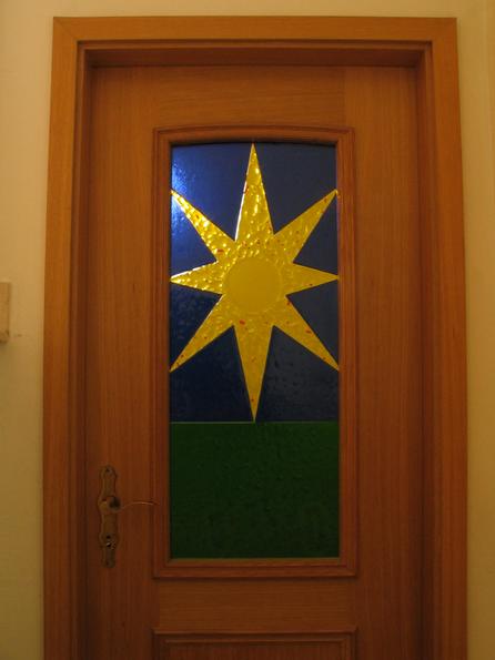 Glas art with melted glas
The glas picture on the door is a symbol for the solar house. Green gras, blue sky and the sun. The colored glas parts are mlted together to on piece.
